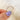 Gold ring held by a hand with purple nail polish on a soft white background