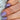Close-up of a hand with a diamond ring and purple nail polish on a textured surface.