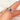 cornflower blue sapphire three stone ring on pointer finger and white background